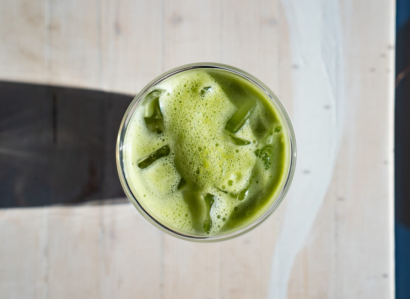 An iced matcha latte seen from above on a white wooden table